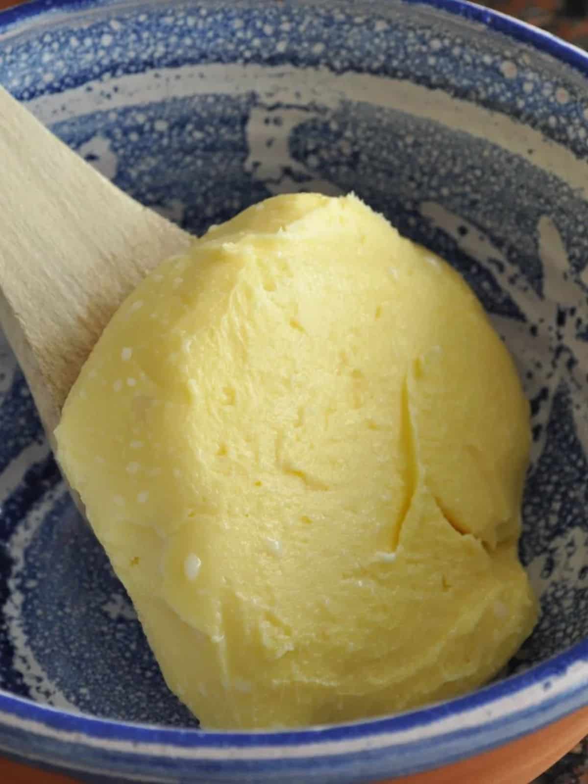 Homemade vanilla butter in a blue bowl sitting on a wooden spoon (1)