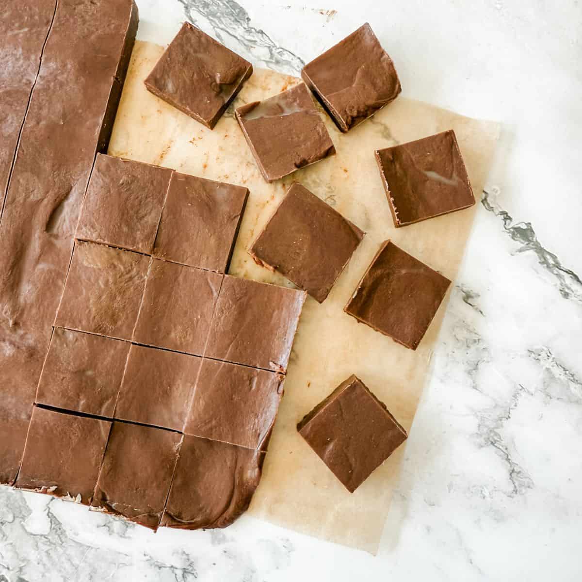 Squares of chocolate cinnamon fudge on brown baking paper on white bench top.