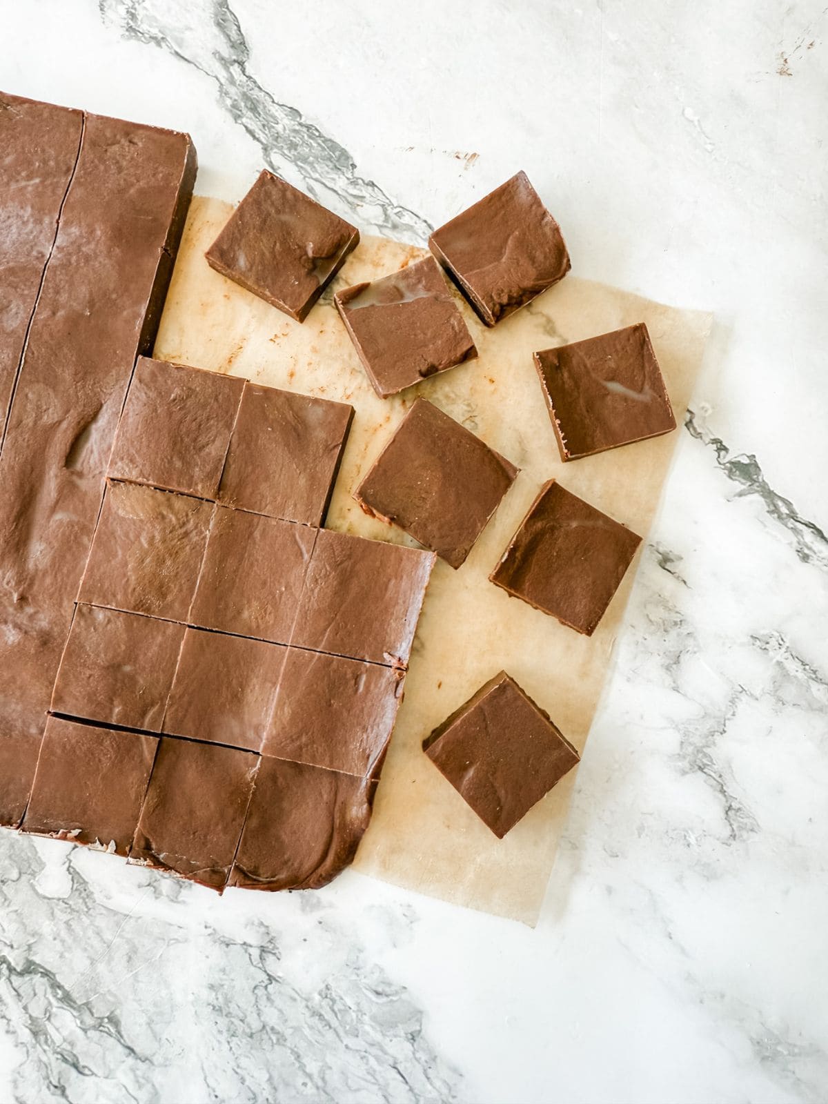 Squares of chocolate cinnamon fudge on brown baking paper on white bench top. 
