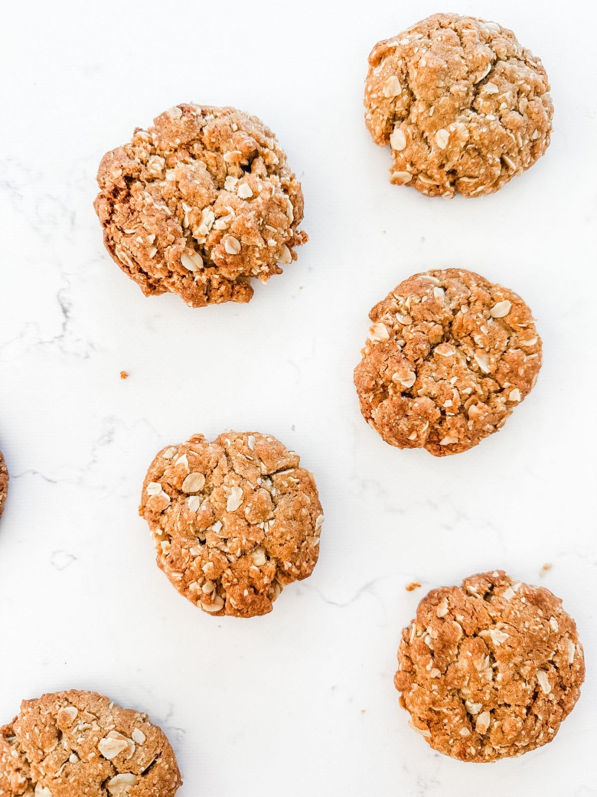 ANZAC Biscuits - biscuits with oats on a white marble bench top.