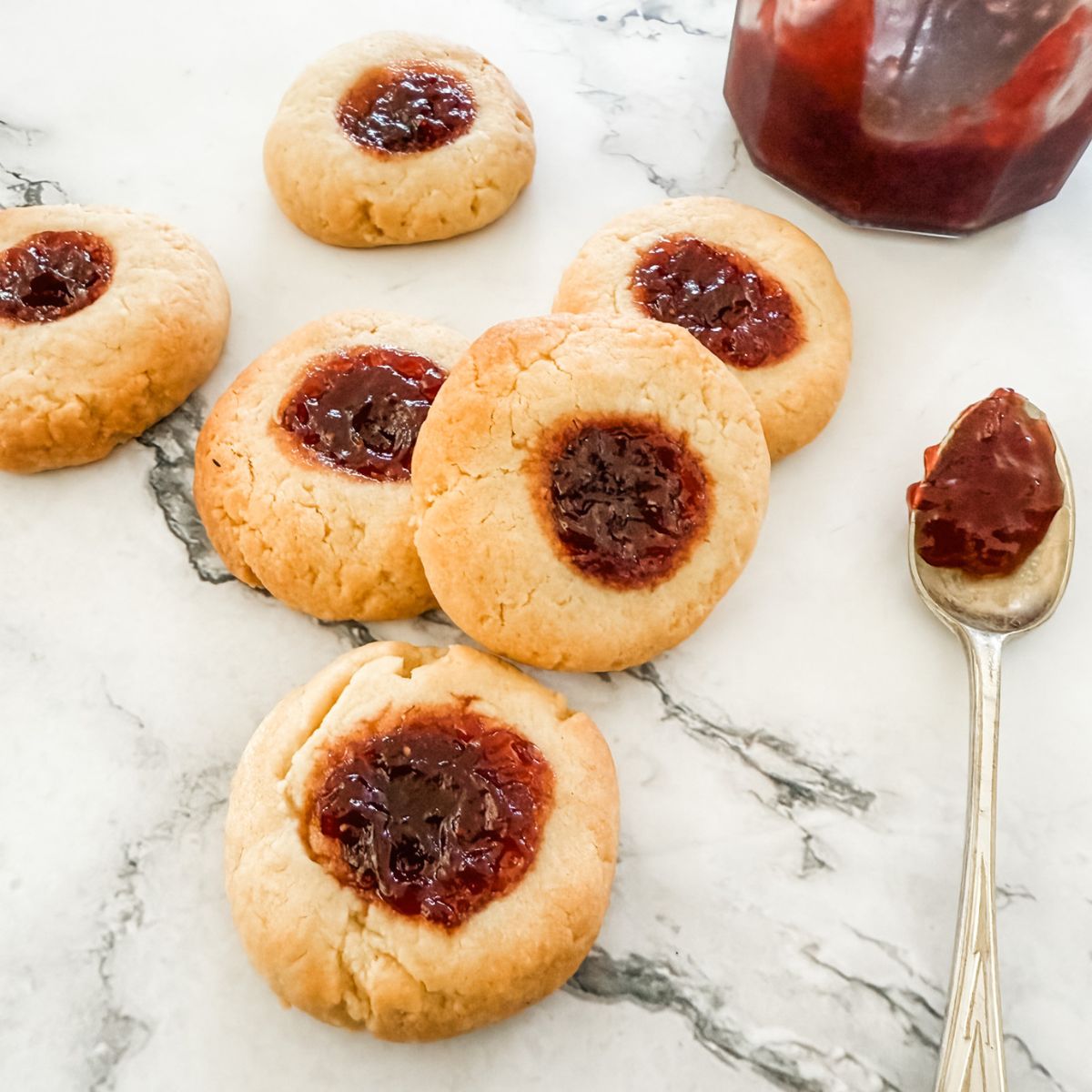 Strawberry Jam Drop Cookies on bench top with spoon of strawberry jam.