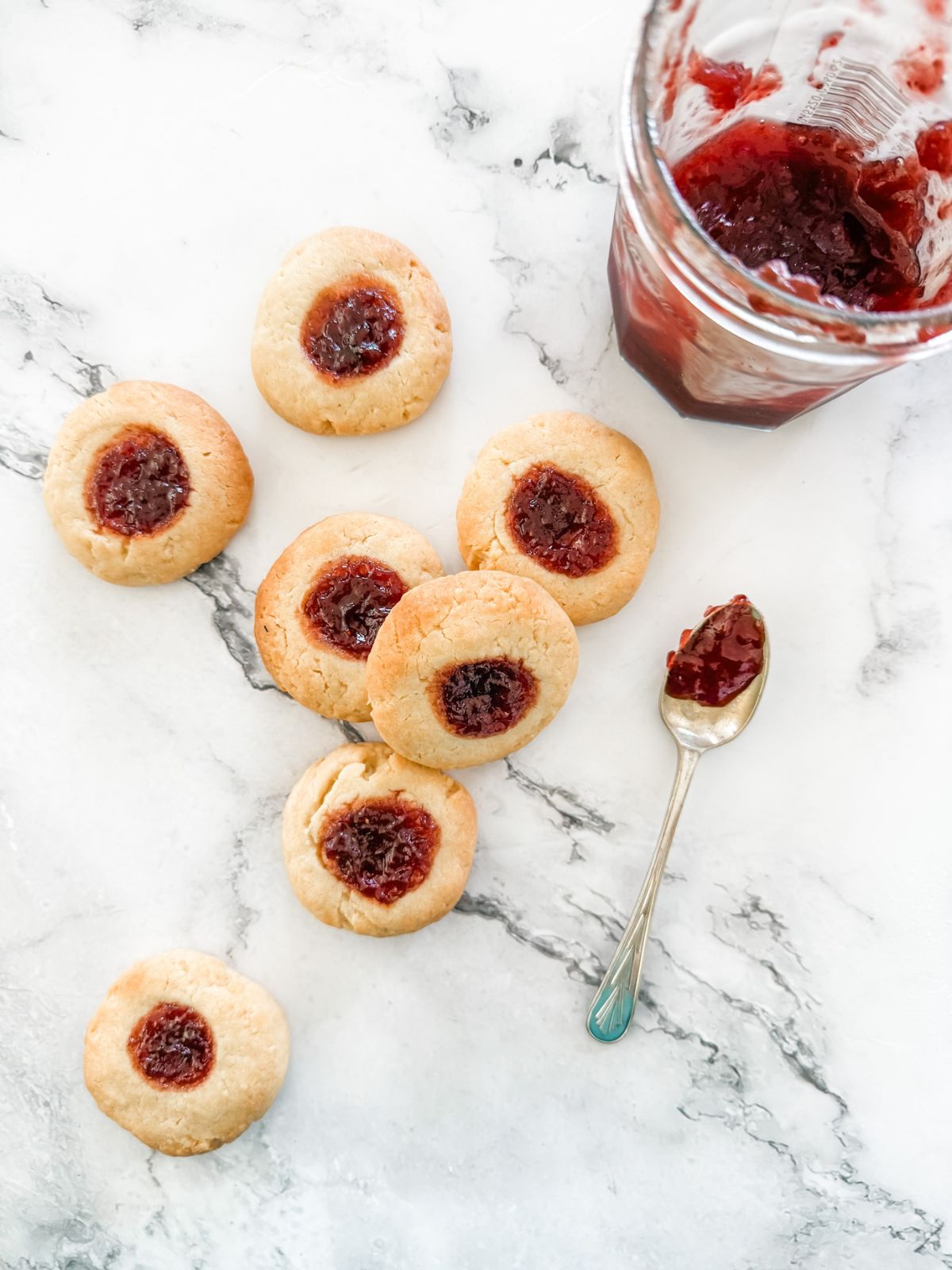 Strawberry jam drop cookies on white marble benchtop with jar of strawberry jam.