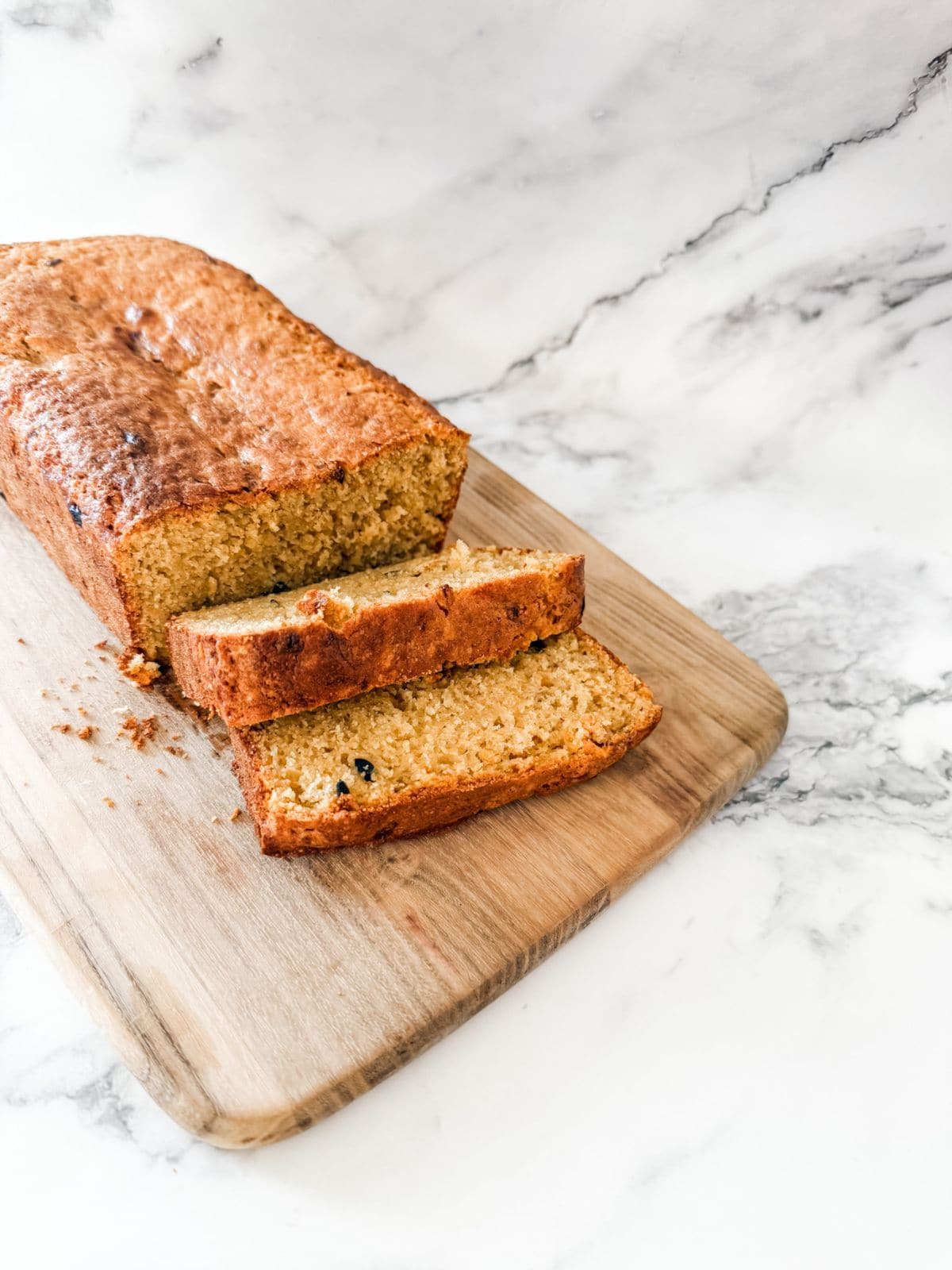 Banana and passion fruit loaf - two slices cut on wooden chopping board on white marble bench.