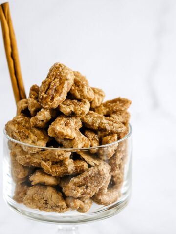 Candied cinnamon pecans in a glass bowl with cinnamon quill.