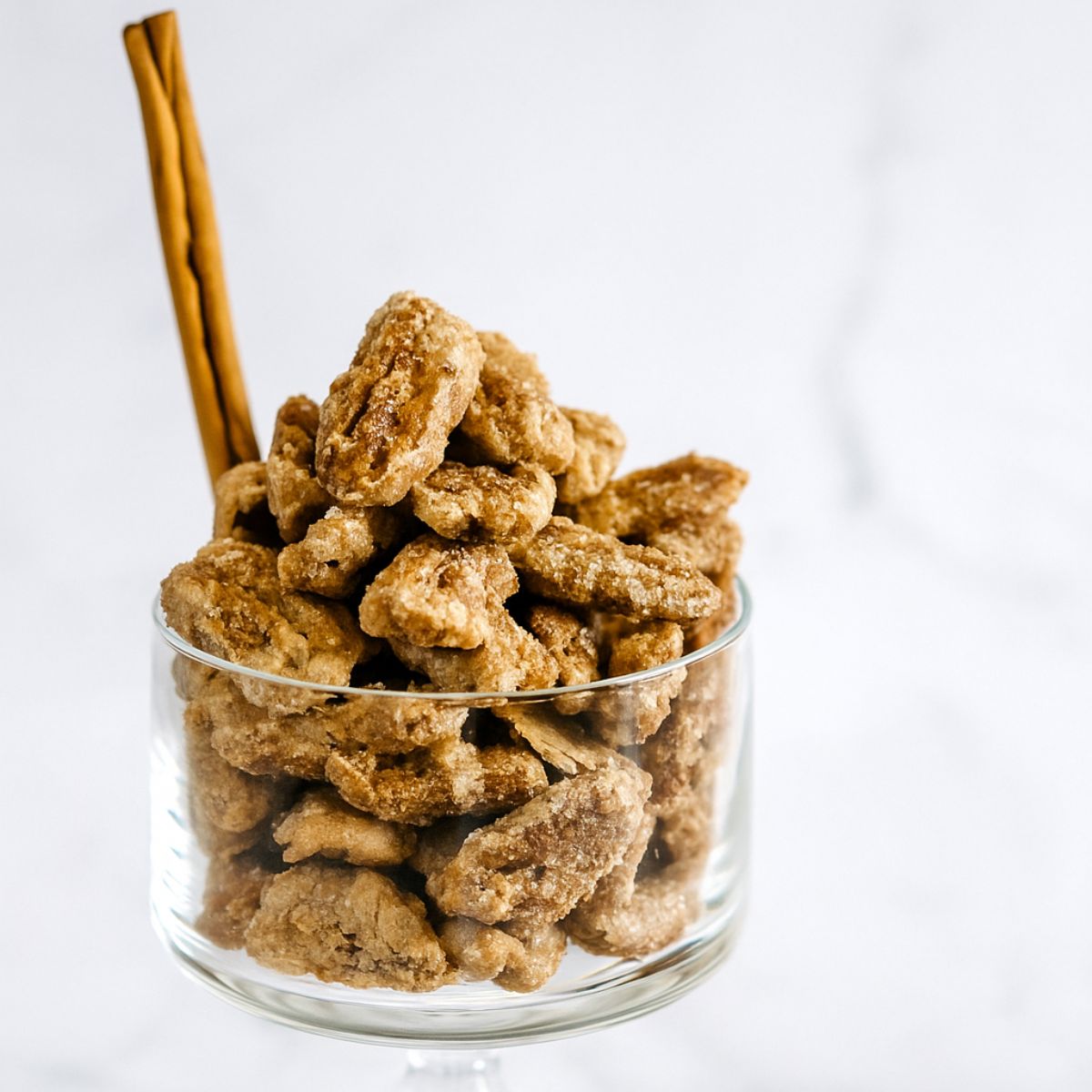 Candied cinnamon pecans in a glass bowl with cinnamon quill.