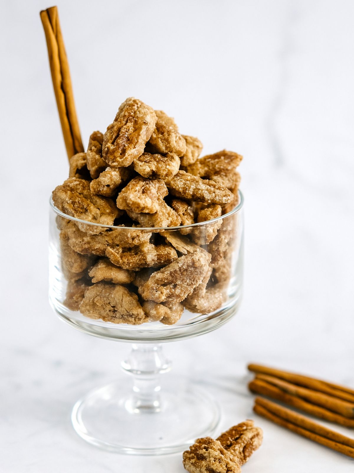 Candied cinnamon pecans in a glass bowl with cinnamon quill.