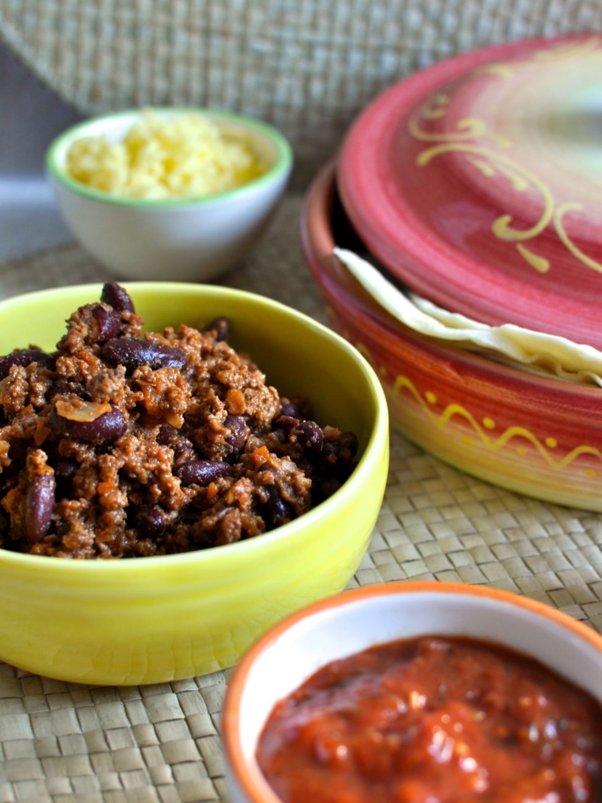 Beef burrito mince in yellow bowl. Tortillas in warmer, salsa in a bowl and shredded cheese in bowl.
