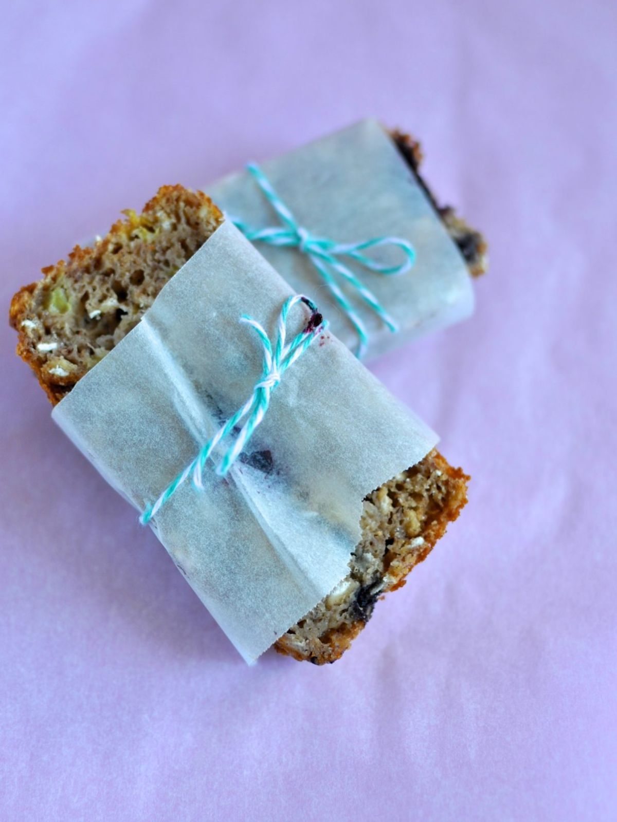 Two slices of banana bread wrapped in white baking paper tied with blue string. 