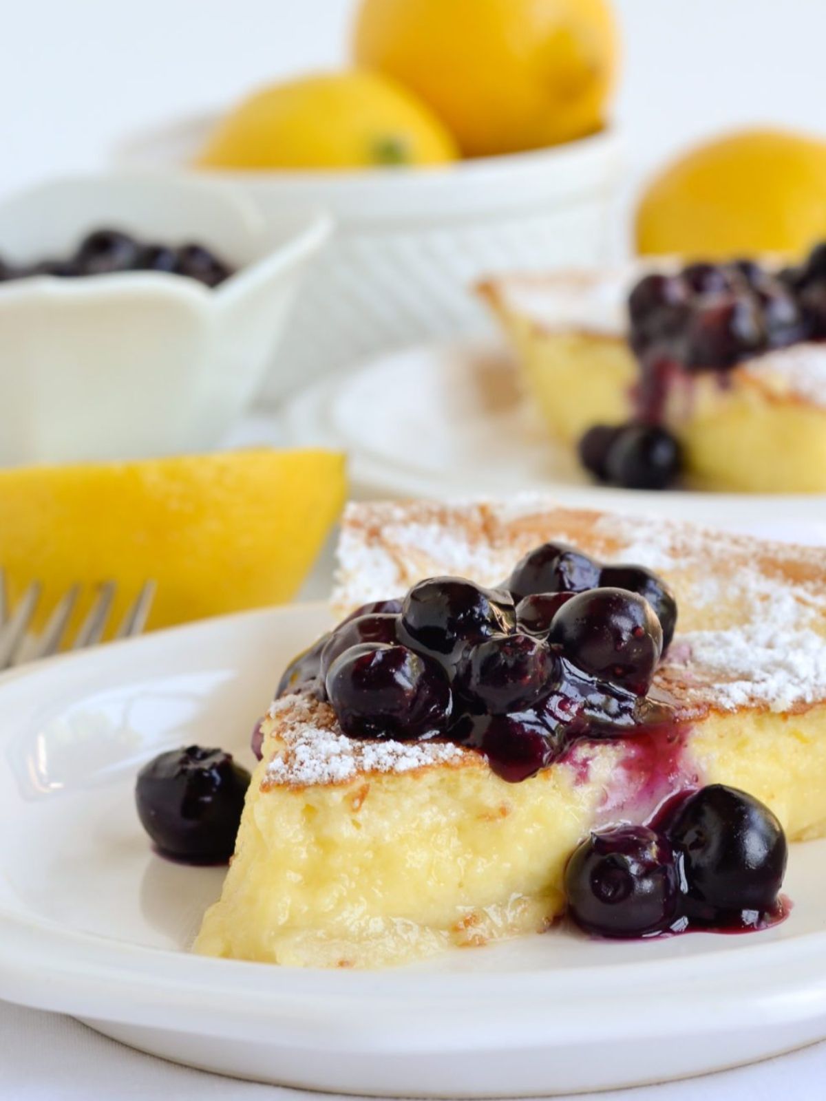 Slice of lemon pie cake with blueberry compote on a white plate. 