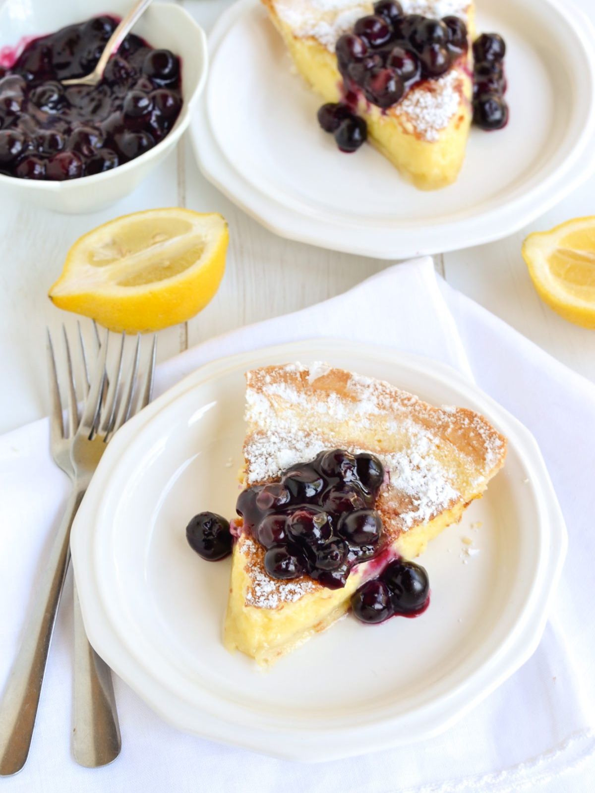 Slice Of Lemon pie cake with blueberry compote on a white plate.