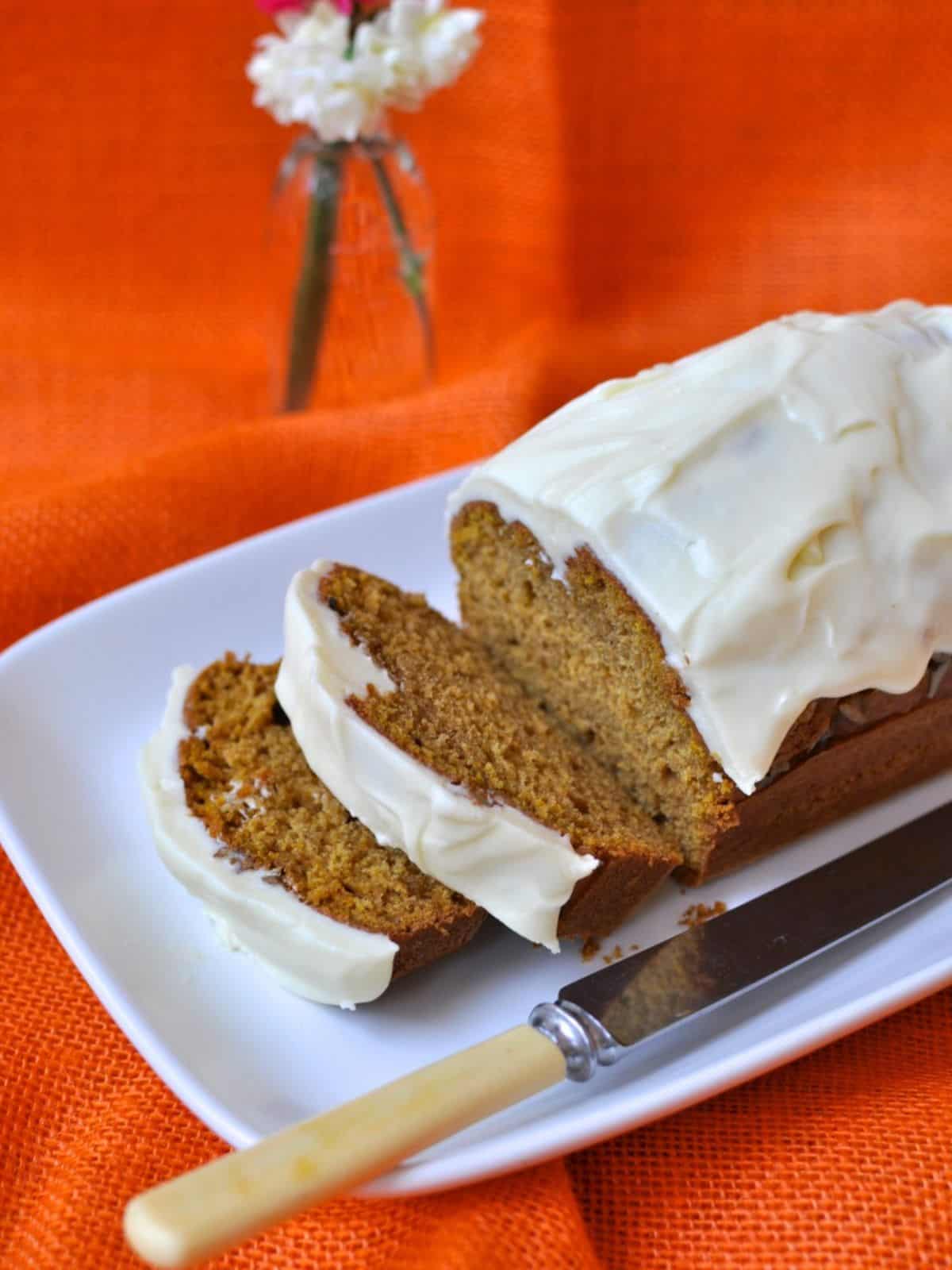 Sliced Pumpkin Bread With Cream Cheese Frosting on white plate.