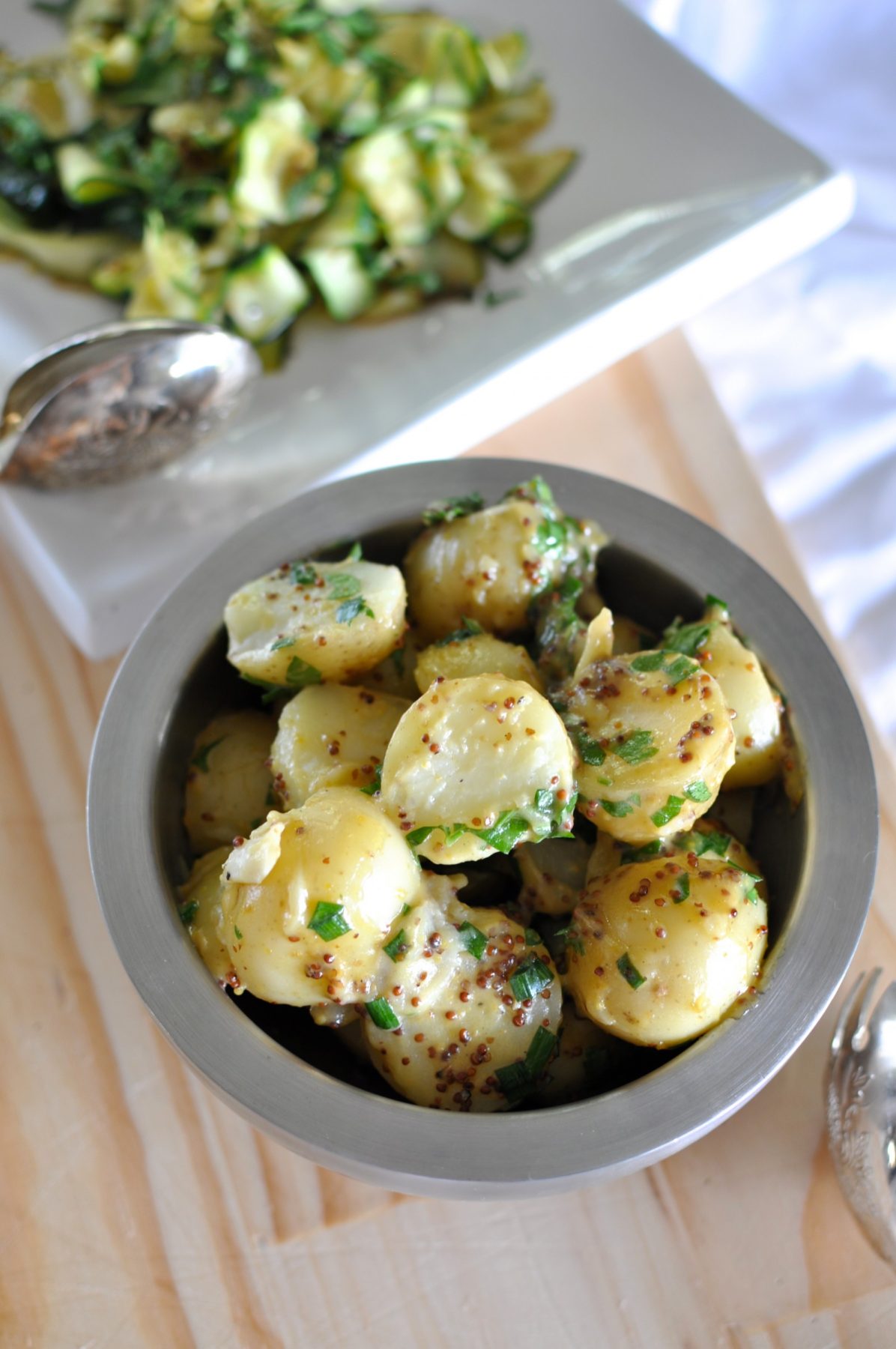Vegan potato salad (a healthy version) in a bowl served next to raw zucchini salad with tongs