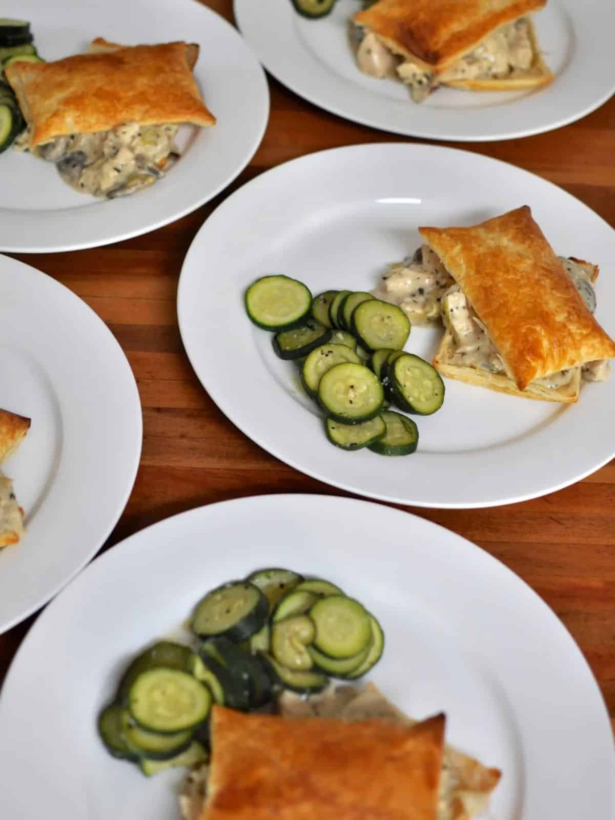 4 white plate of tarragon chicken in squares of puff pastry with steamed zucchini
