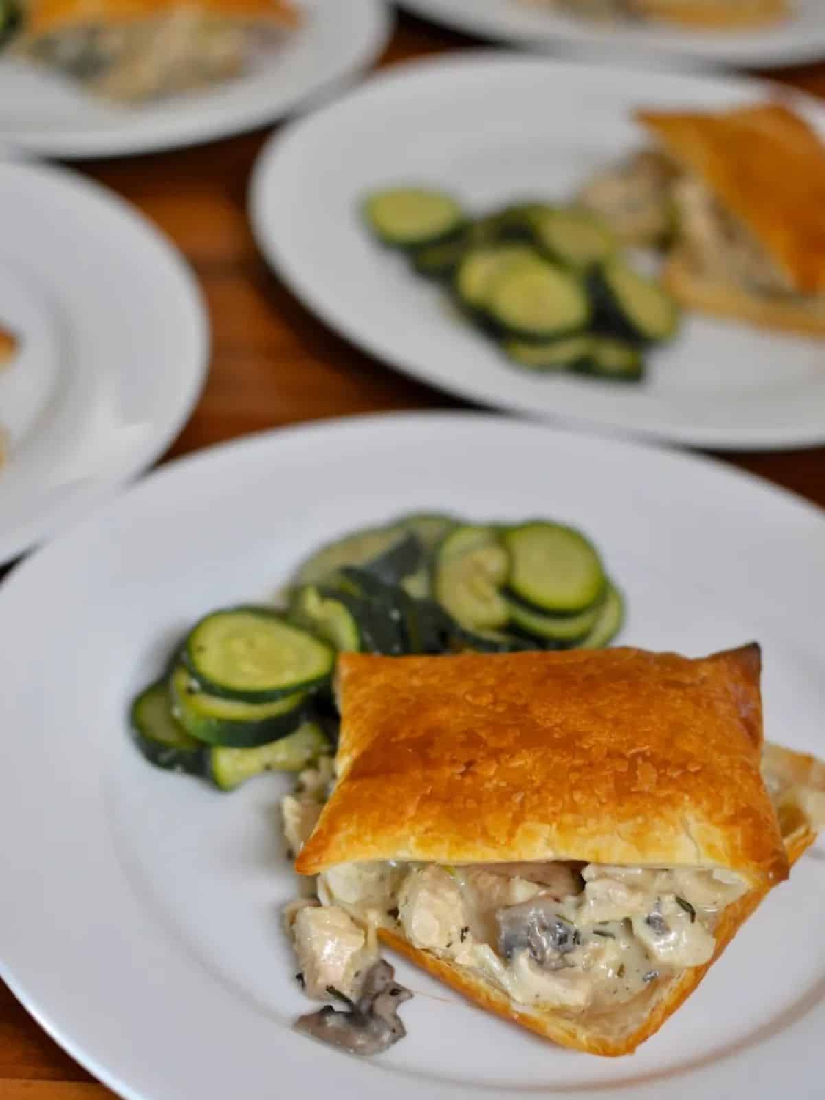 2 white plates of tarragon chicken in puff pastry squares with steamed zucchini