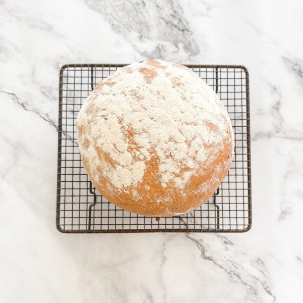 Freshly baked olive bread coated in flour cooling on a wire rack.
