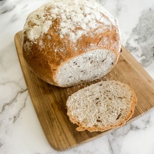 Olive bread on a wooden chopping board on a marble bench top. The end has been sliced.
