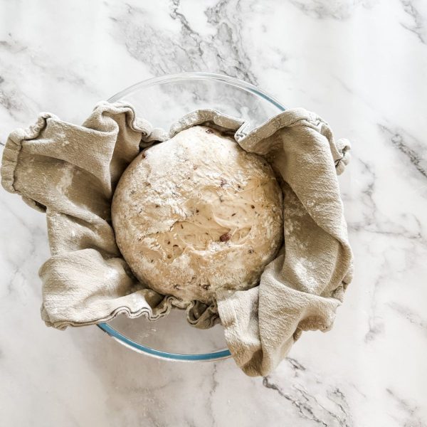 Olive bread dough ball risen in a tea-towel lined glass bowl