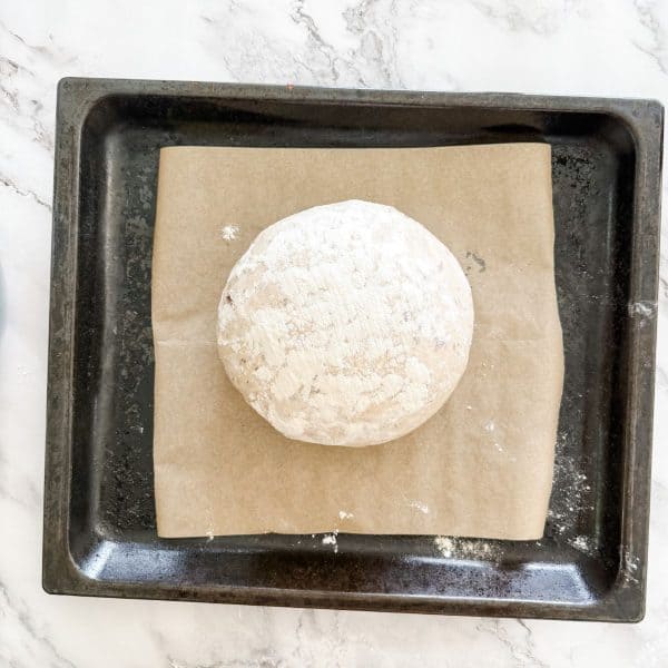 Ball of olive bread dough on a baking paper lined oven tray ready for baking. 