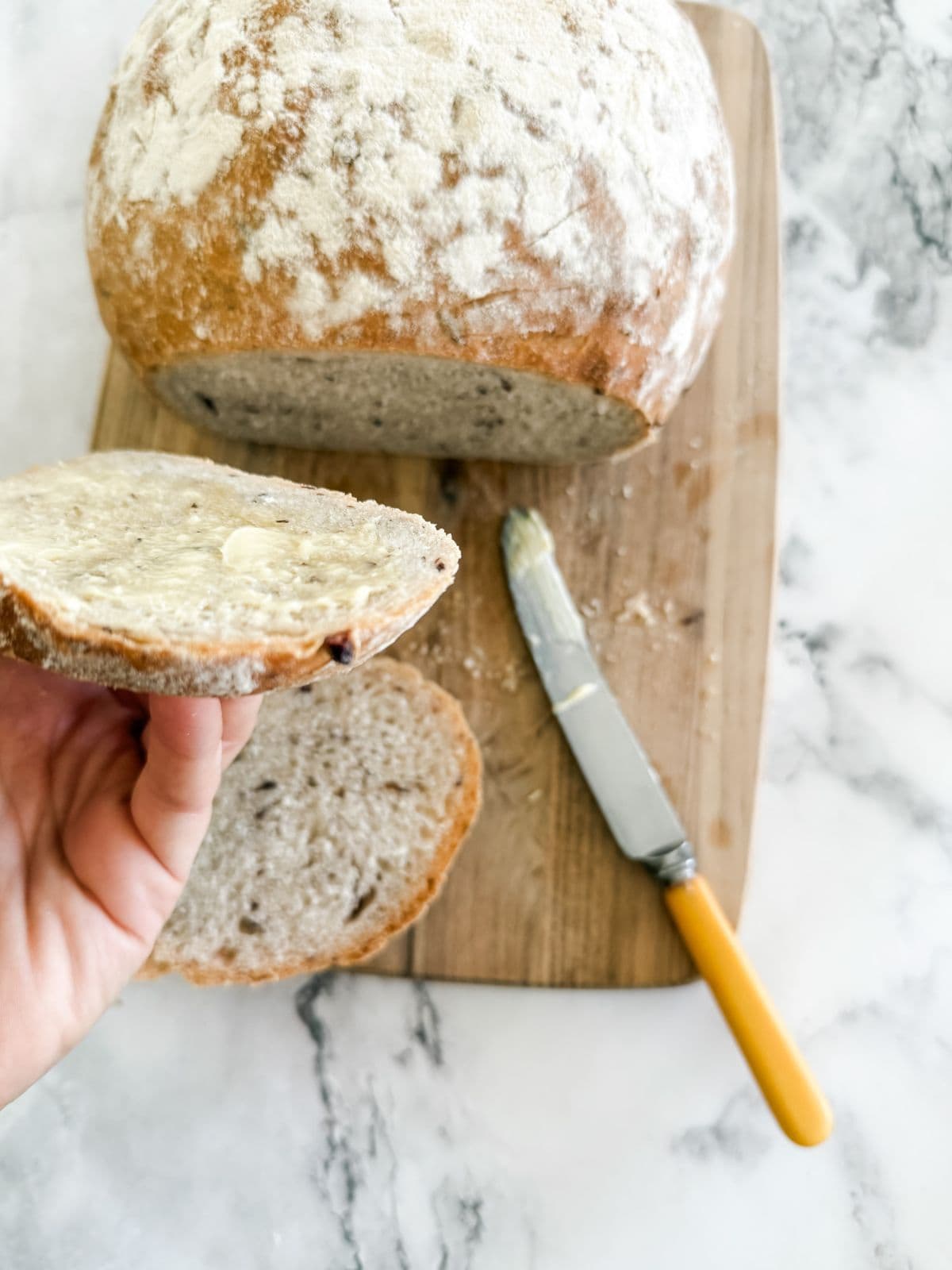 Olive bread on wooden board with slice cut out spread with butter. 