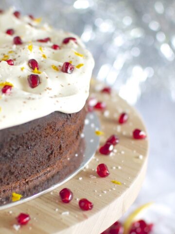 Chocolate cake on timber cake stand iced with white icing topped with pomegranate & orange zest.