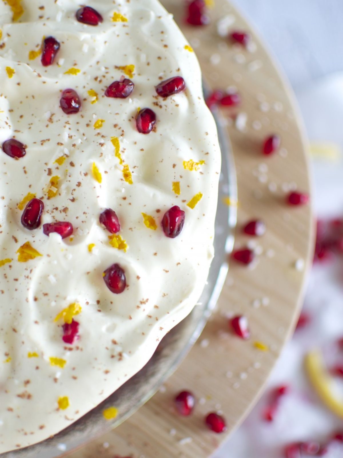 Chocolate cake on timber cake stand iced with white icing topped with pomegranate & orange zest.