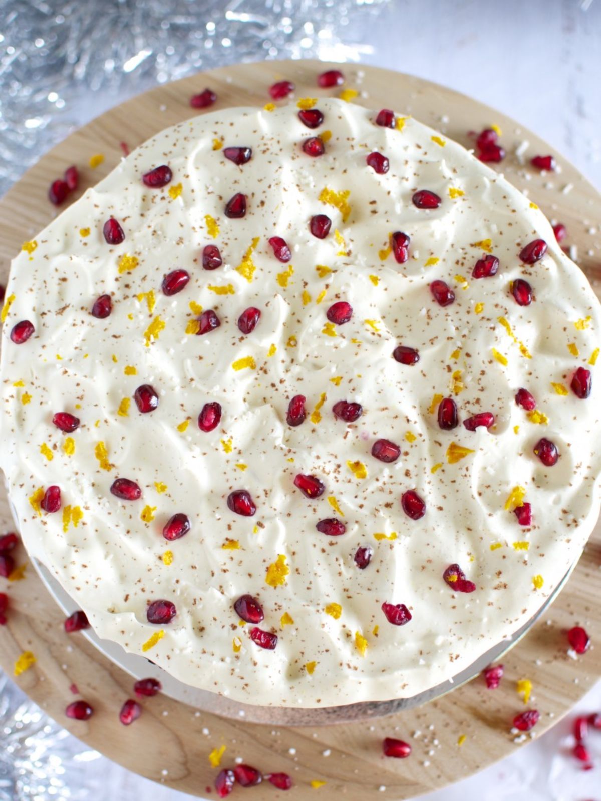 Chocolate cake on timber cake stand iced with white icing topped with pomegranate & orange zest.