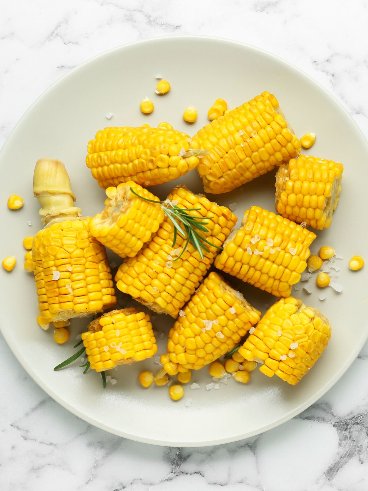 Pieces of cooked corn on the cob with butter on a white plate.
