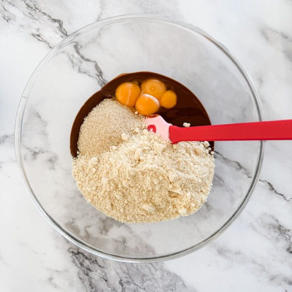 Mixing sugar, almond meal and egg yolks into melted chocolate and butter