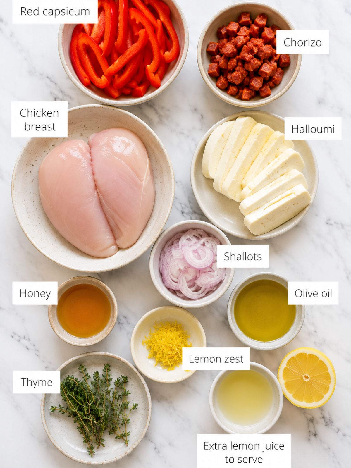 Bowls of ingredients for making Chicken chorizo and halloumi bake laid out on a white marble bench top.