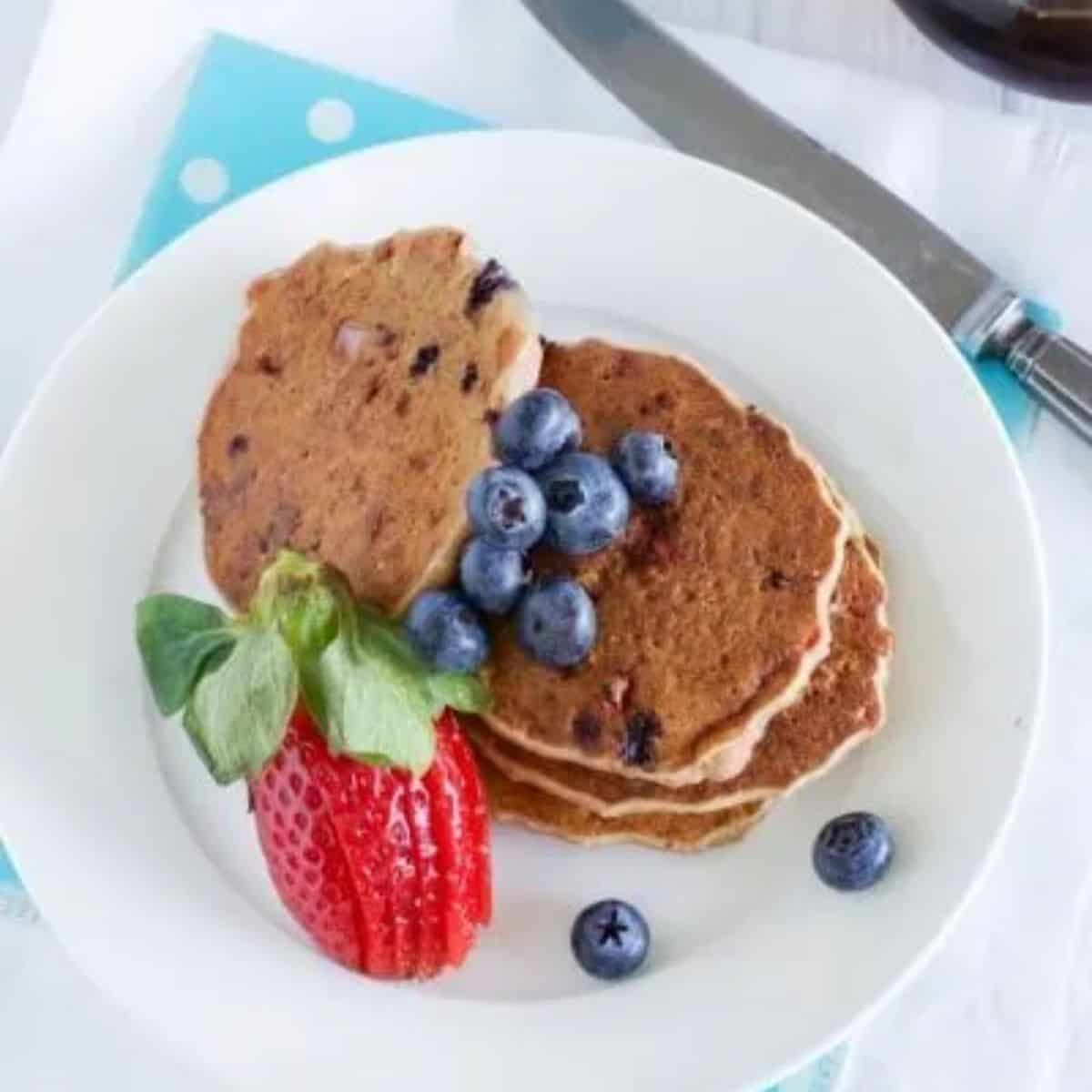 Egg free berry pancakes on a white plate with fresh blueberries and a strawberry