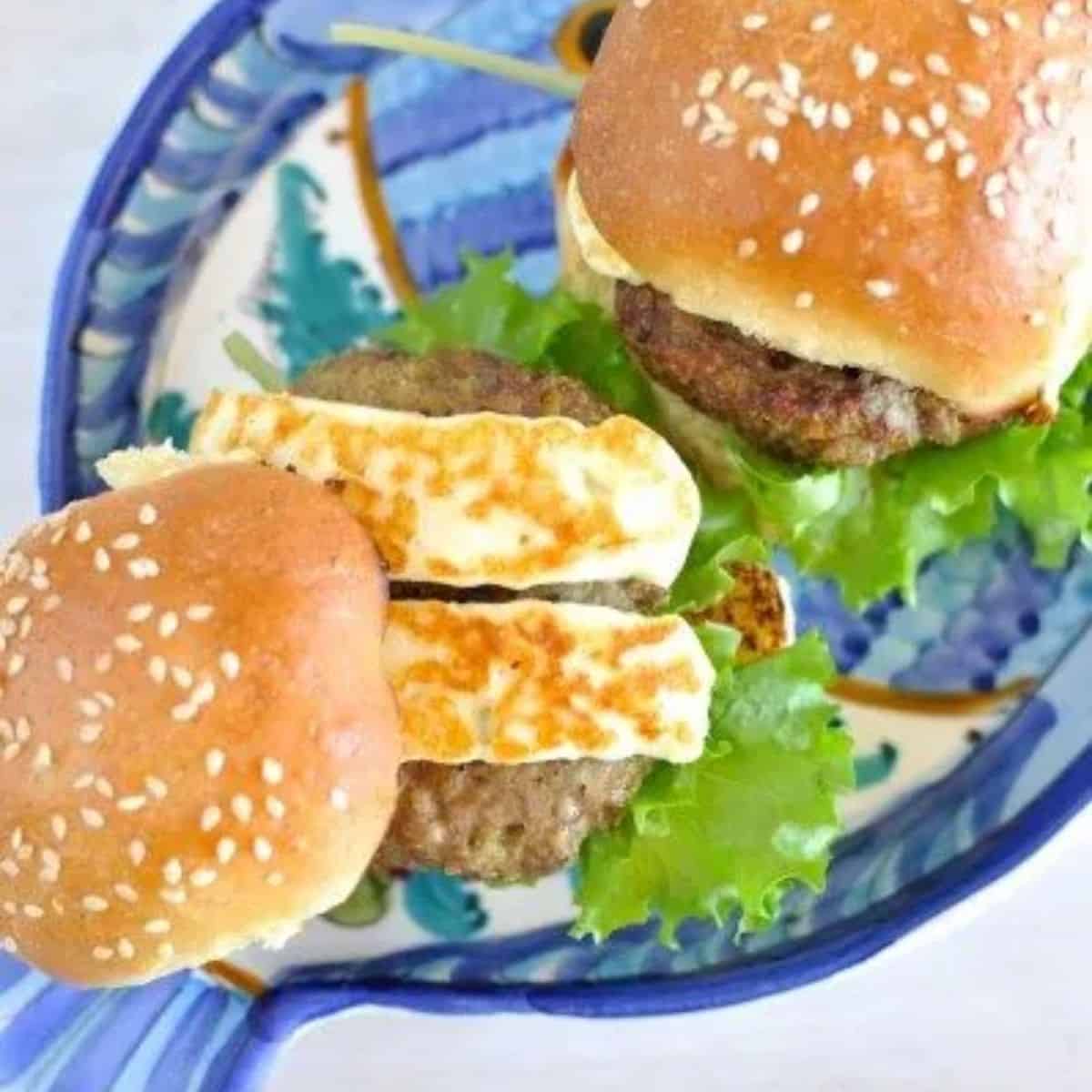 Greek lamb and haloumi burgers - two burgers on a fish-shaped plate. One open showing the meat pattie and two strips of halloumi inside.
