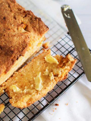 Pumpkin and feta loaf with one slice sliced off the end on its side spread with butter. Also pictured an old ivory handled butter knife.