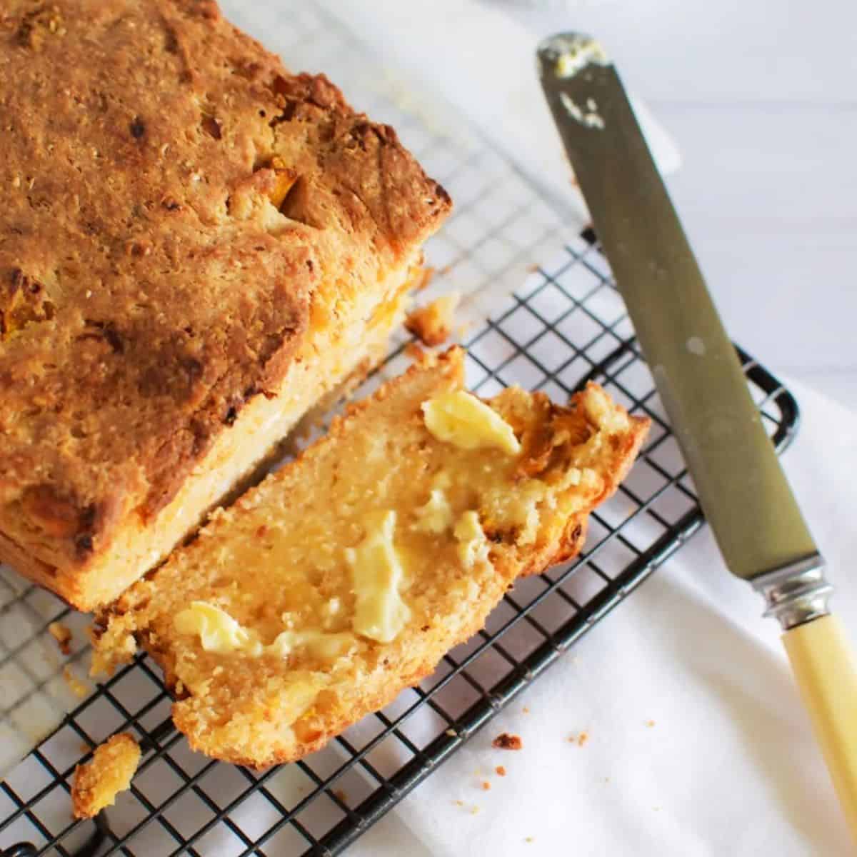 Pumpkin and feta loaf with one slice sliced off the end on its side spread with butter. Also pictured an old ivory handled butter knife.