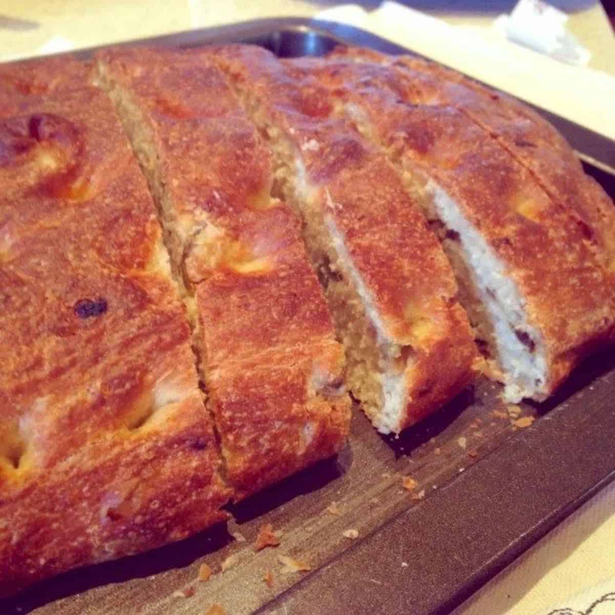 Caramelised onion focaccia with olives - loaf sliced on wooden chopping board.