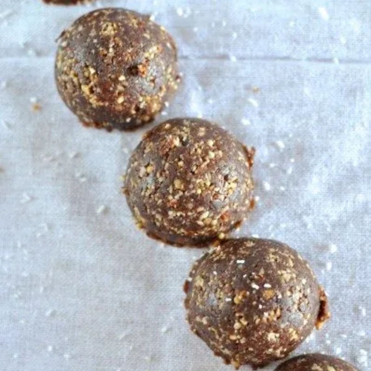 Choc ginger nut and seed balls - half balls of chocolate seed mix on white backdrop sprinkled with coconut.