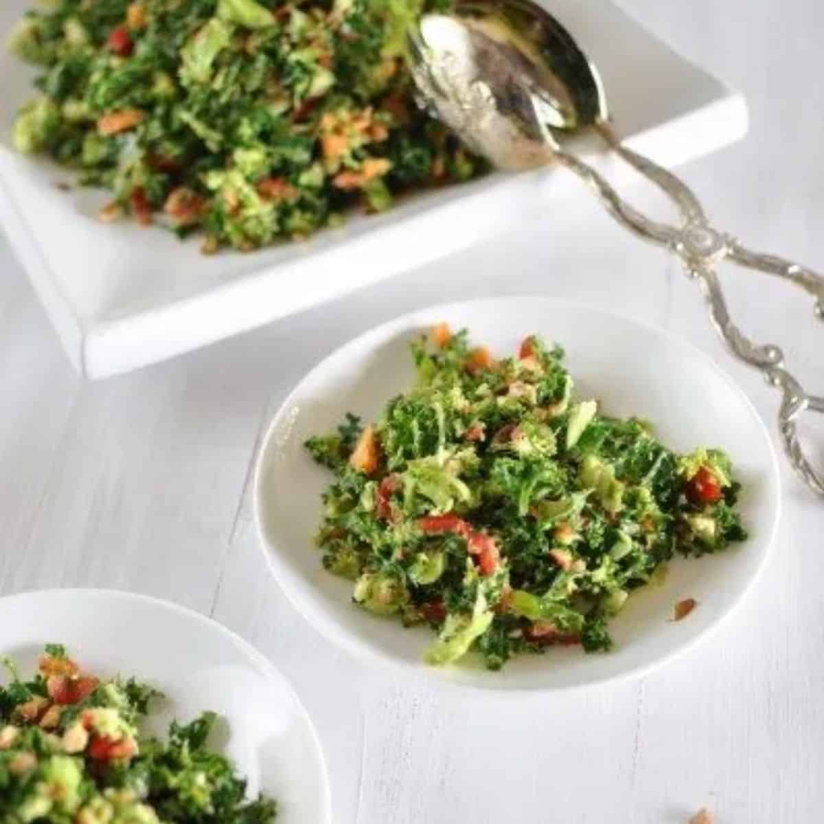 Fresh vegetable chopped salad on bowl after being served with silver tongs from a white square plate.