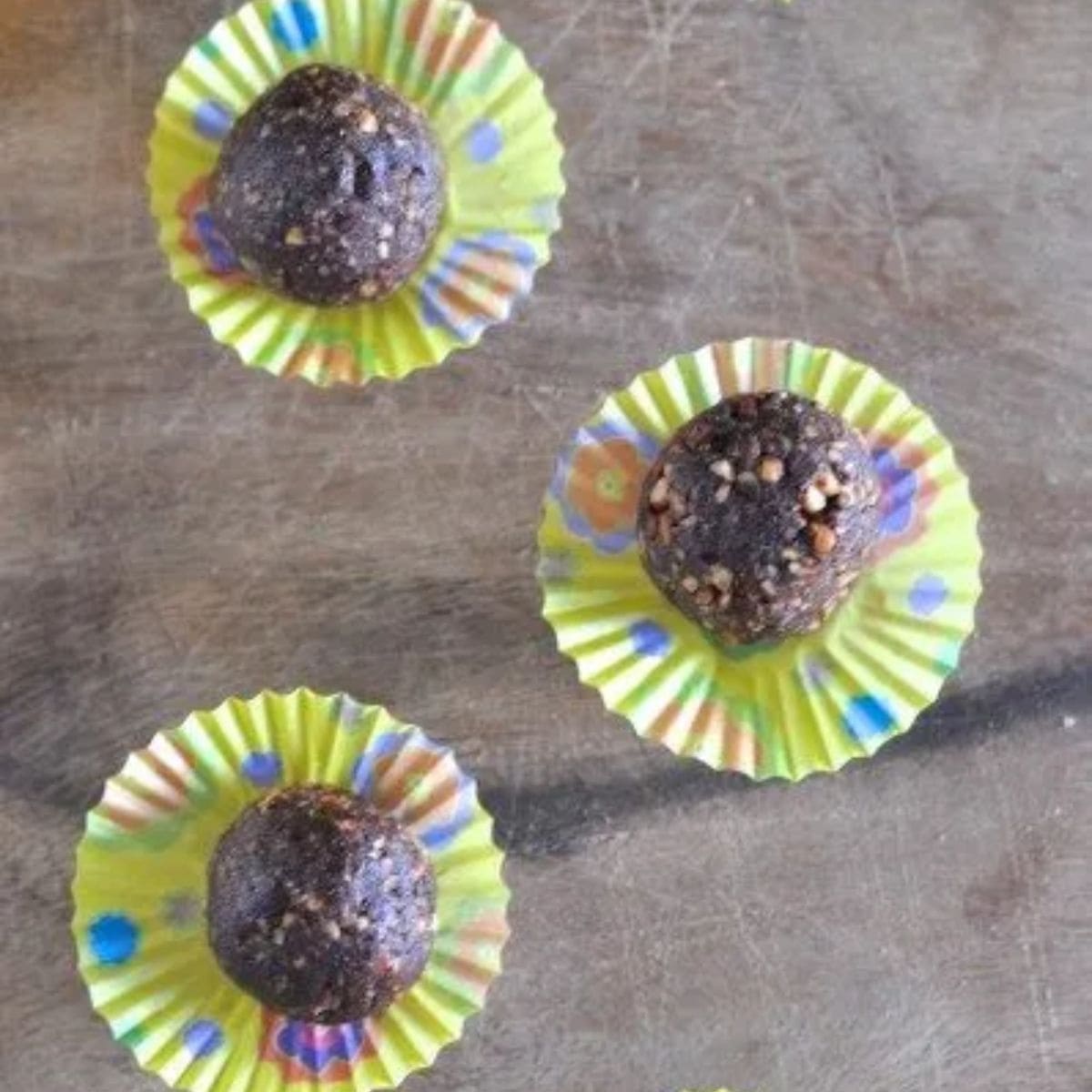 Paleo chocolate almond balls - chocolate coloured balls on yellow flattened cupcake wrappers on a brown wooden board.