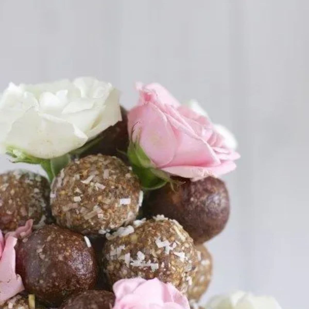 Choc almond and rosewater bliss balls in a tower with white and pink fake roses.
