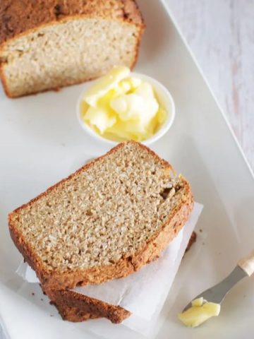 Coconut bread sliced on a white plate with a ramekin of butter and a small butter knife.