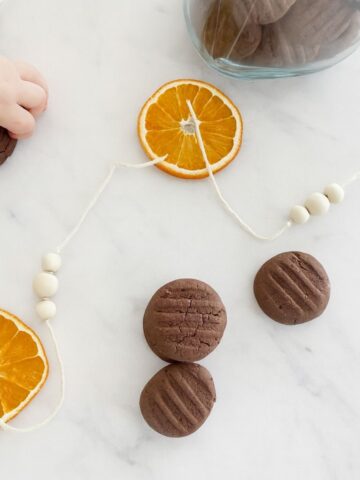 4 Chocolate shortbread Christmas Cookies on white marble benchtop with jar of cookies.