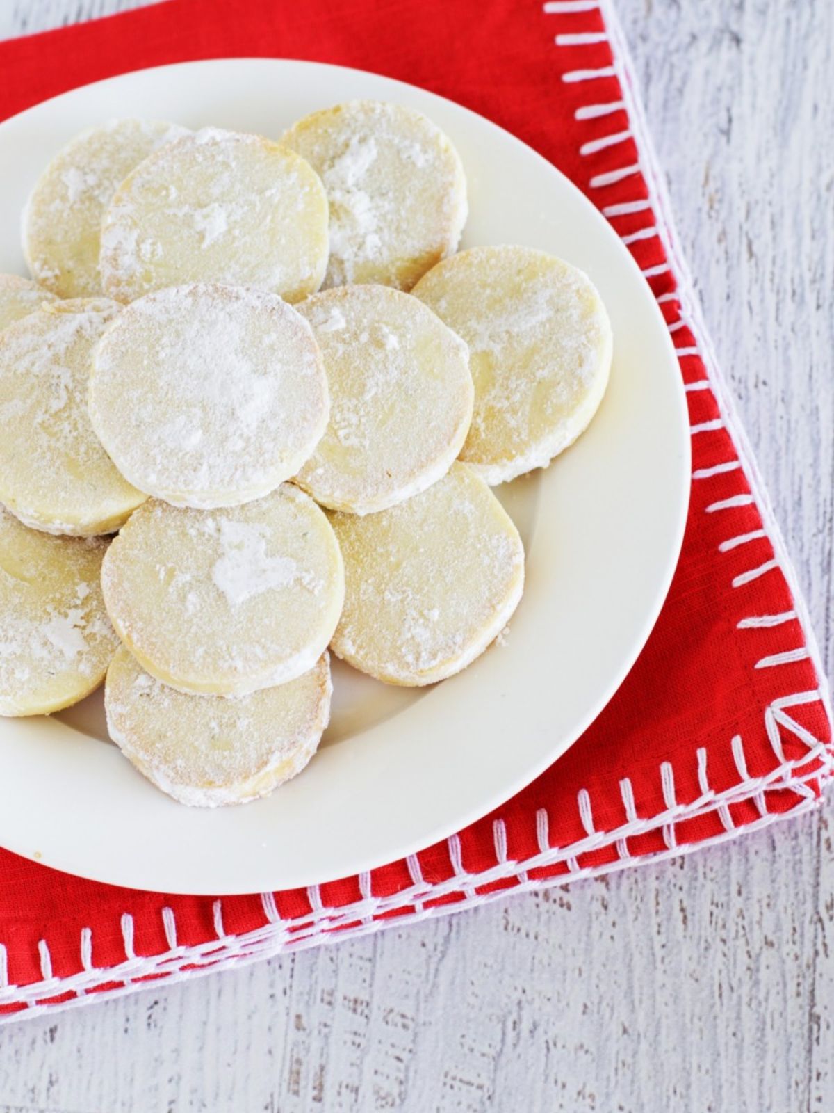 Lime meltaway shortbread cookies on plate on red napkin on white benchtop. 