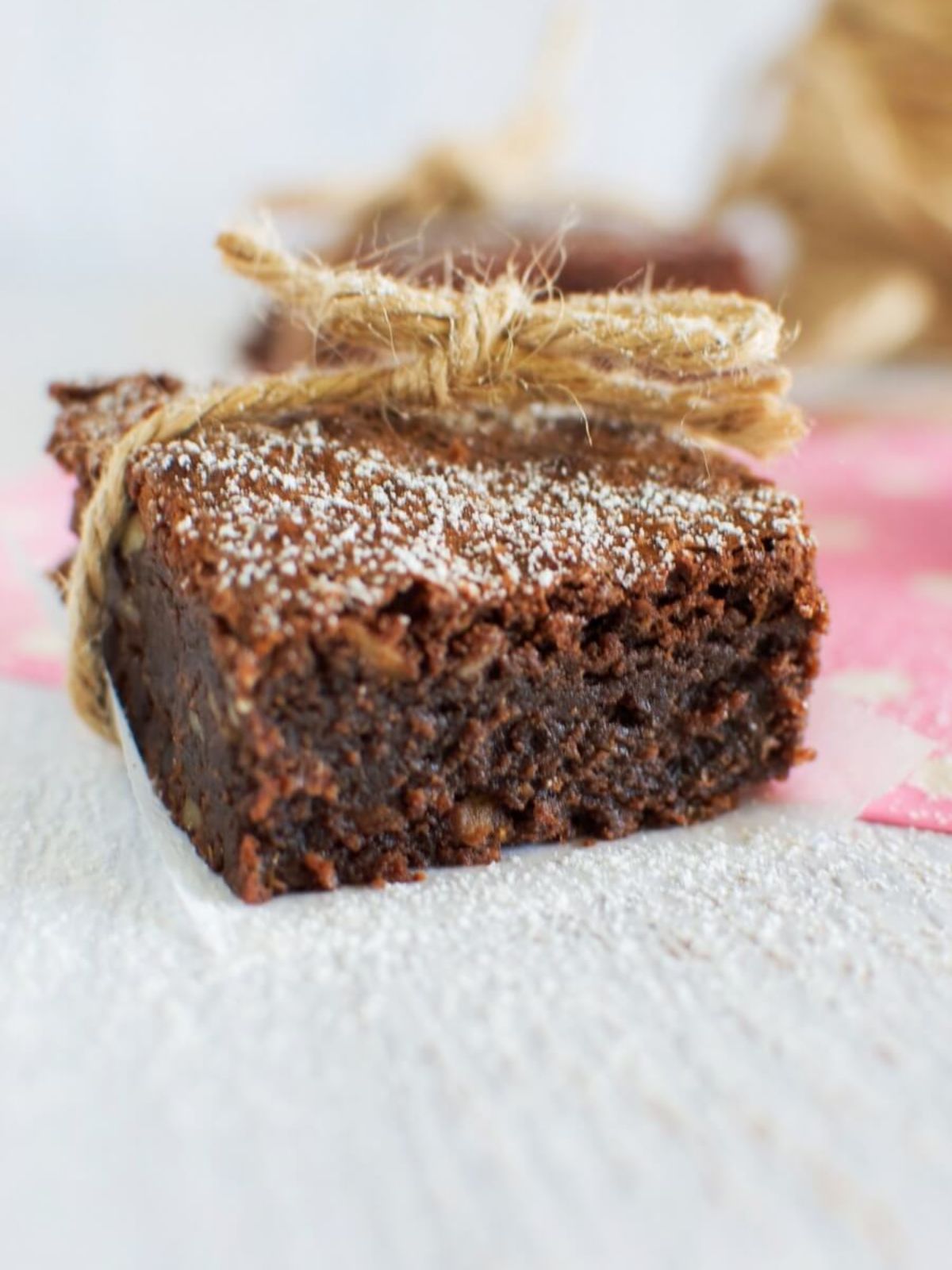 Square of chocolate brownie tied with twine on pink and white napkin.