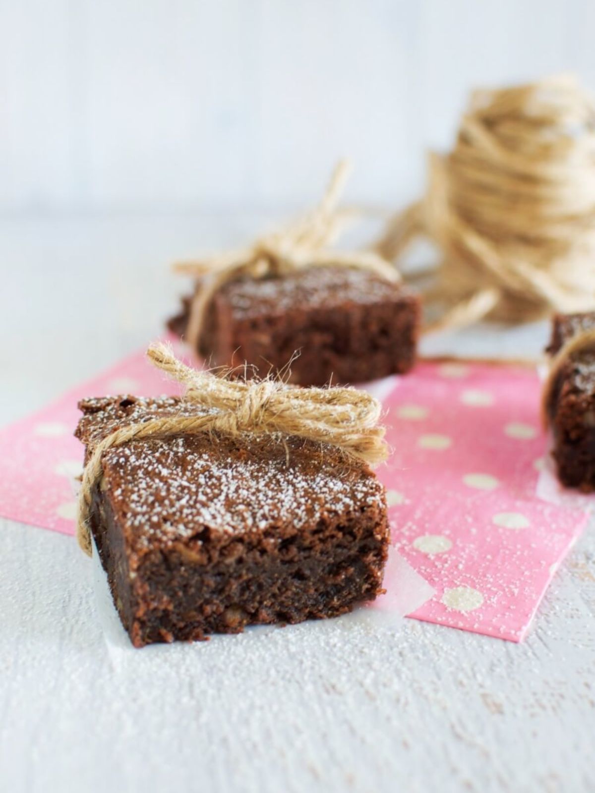 Chocolate brownie square with icing sugar and a twine bow on pink spotty napkin. 