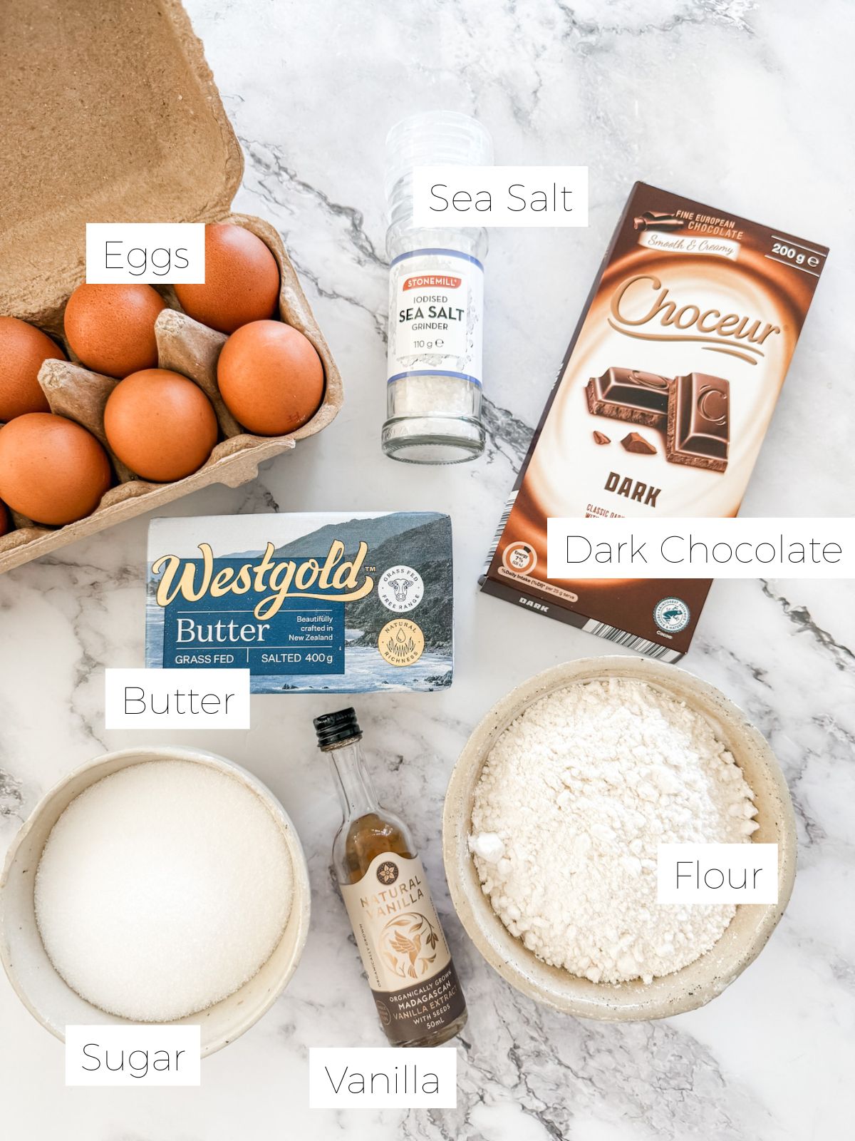 Ingredients in Best Ever Chocolate Brownie Recipe - chocolate, sugar, flour, eggs, vanilla & salt on white marble bench. 