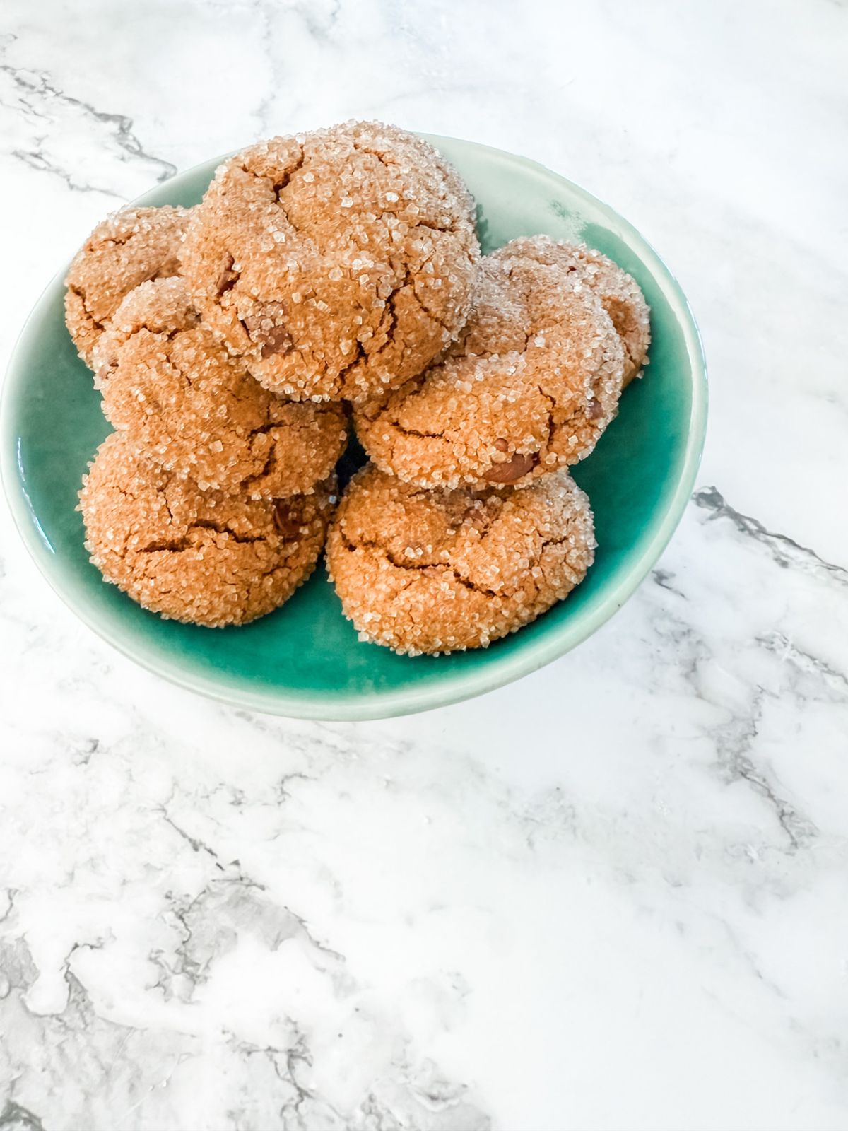 Chocolate ginger cookies coated in sugar on a teal small cake stand on white marble bench top. 
