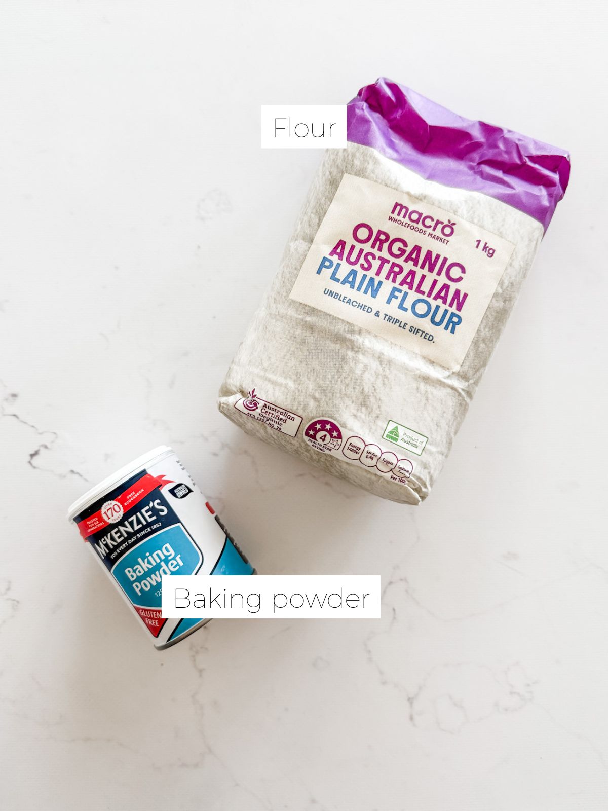 Bag of flour and tin of baking powder on white marble bench.