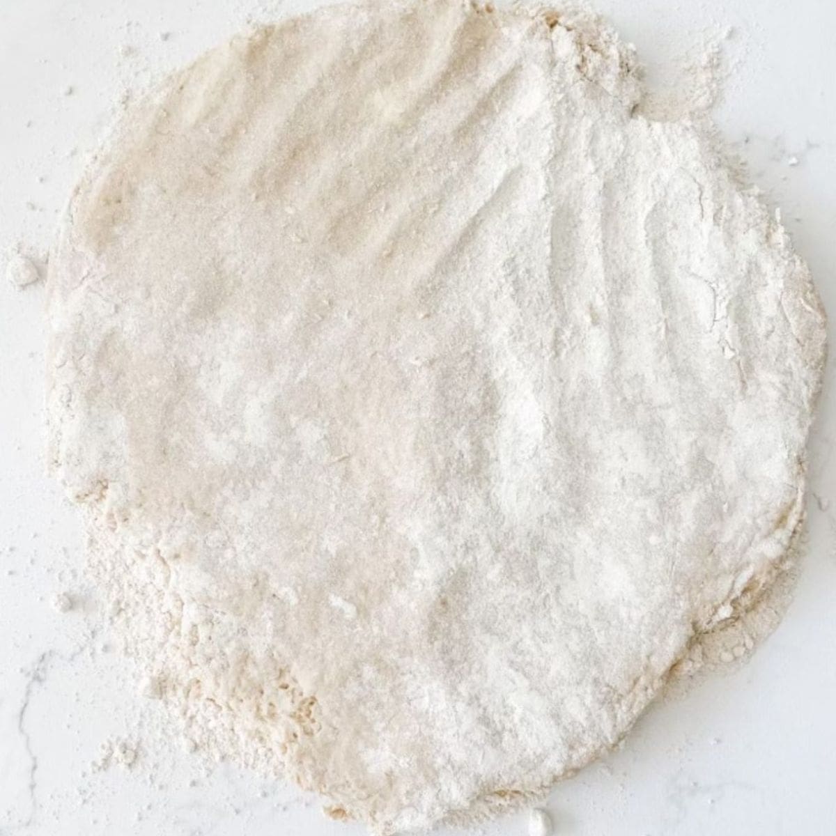 Scone dough patted out on white marble bench top. 