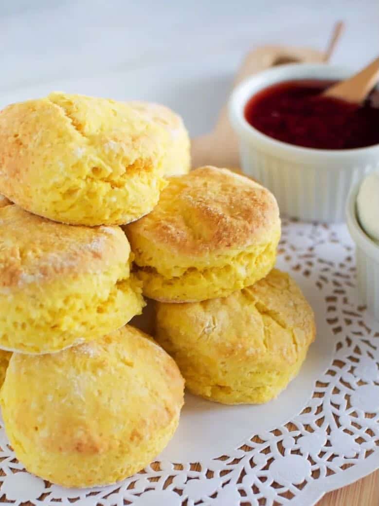 Pile of pumpkin scones on a paper doile with raspberry jam in the background