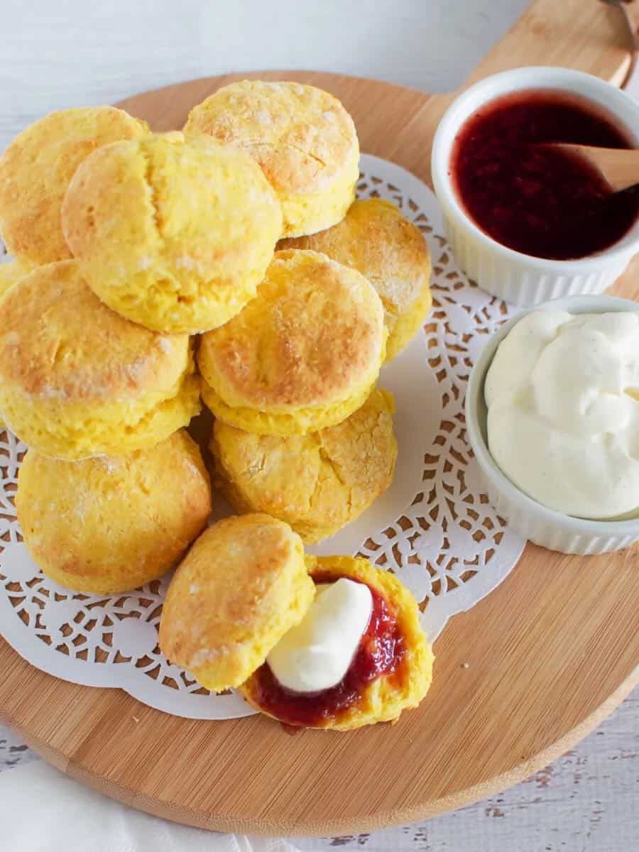 Top view of pumpkin scone cut in half with strawberry jam and cream on top. A oile of pumpkin scones in the background.