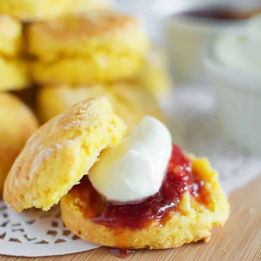 Pumpkin scone cut in half with strawberry jam and cream on top. A oile of pumpkin scones in the background.
